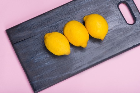 lemons on a wooden board. citrus on a black cutting board. Healthy food. Vitamins. Pink background. background color Pink Lavender.の写真素材