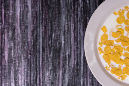 Corn flakes with milk. Plate on a wooden background. White dish with flakes. Yellow flakes. Salvage is a waste. Wooden multicolored background.の写真素材