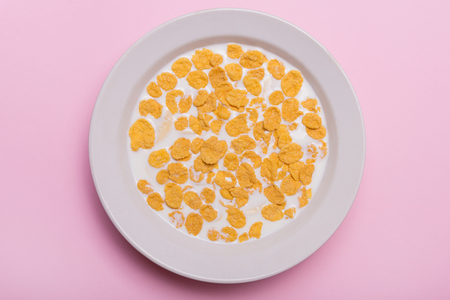 Yellow flakes. Sunflower with flakes and milk. Sweet breakfast. Quick breakfast. Flakes with milk. Flakes in a white plate. Pink background. Pink Lavenderの写真素材