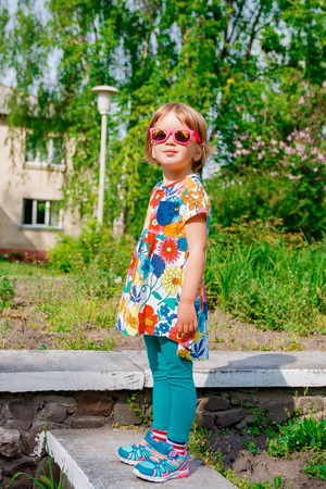 cute little girl in pink sunglasses and flower dress standing outdoorsの写真素材