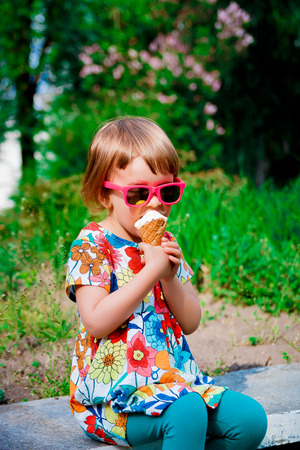 Cute and happy little girl in pink sunglasses sitting and eating ice cream outdoor. Yummy ice creamの写真素材