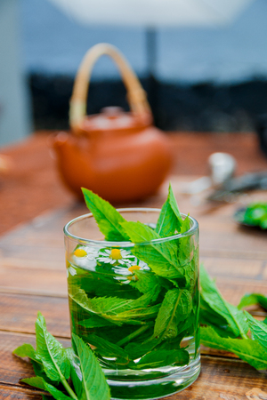 A cup of mint tea with chamomile on a wooden background. herbal tea with chamomile and fresh mint leaves on table.の写真素材