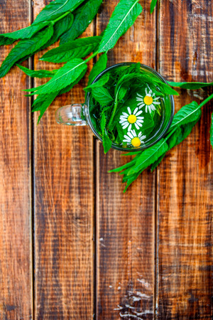 A cup of mint tea with chamomile on a wooden background. herbal tea with chamomile and fresh mint leaves on table. Copy space. Frame. Top view.の写真素材