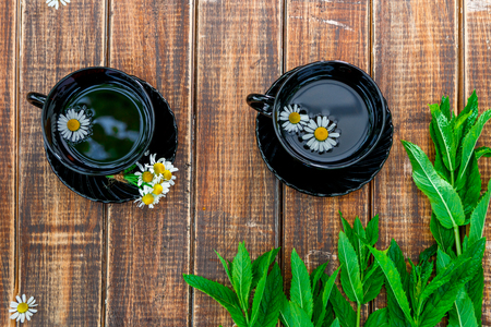 Two black cup of tea with chamomile near fresh mint on wooden table background. Tea concept. Frame, copy space. Top view.の写真素材