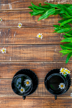 Two black cup of tea with chamomile near fresh mint on wooden table background. Tea concept. Frame, copy space. Top view.の写真素材