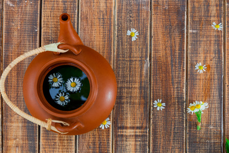 Open brown teapot with tea and flower of chamomile on wooden background. Tea concept. Frame, copy space. Top view.の写真素材