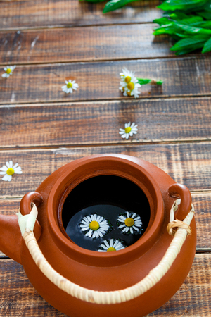 Open brown teapot with tea and flower of chamomile on wooden background. Tea concept. Frame, copy space. Top view.の写真素材