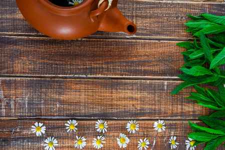 brown teapot with tea near flower of chamomile and fresh mint on wooden background. Tea concept. Frame, copy space. Top view.の写真素材