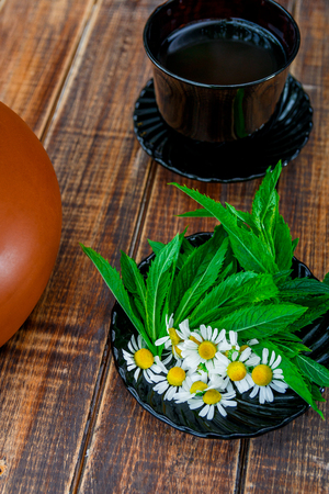 Cup of tea near black plate with fresh mint and chamomile on wooden background. Closeup. Tea concept.の写真素材