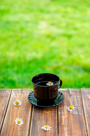 Black cup of tea on wooden with flower of chamomile table  in garden and on nature background. Tea concept.の写真素材