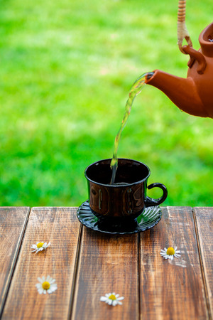 tea pouring into black cup on wooden with fresh chamomile table  in garden and on nature background.の写真素材