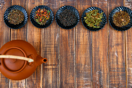 Different kinds of tea on plates near brown teapot on wooden background. Assortment of dry tea. Tea concept. Tea leaves. Frame. Copy space. Top view.の写真素材