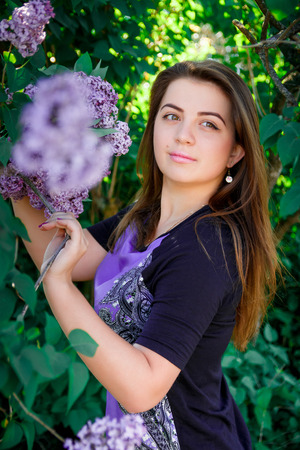 Portrait of Beautiful, long haired, dark-haired girl in purple dress in blooming trees. Attractive romantic woman in flowers of lilac. Warm photo.の写真素材