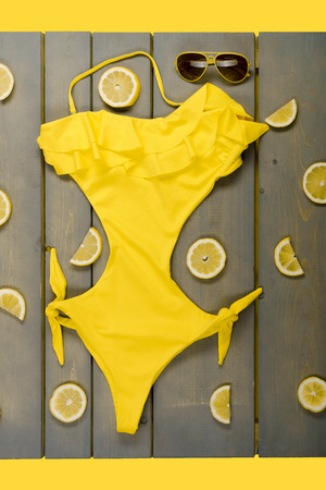 Yellow one-Piece swimsuit, aviator sunglasses between parts of lemons on grey wooden board. Beach accessories on wooden background.の写真素材
