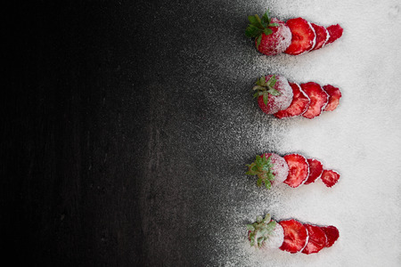 Sliced fresh strawberries powdered sugar  on black background. Top view, frame. Copy space. Summer fruit food frame.の写真素材