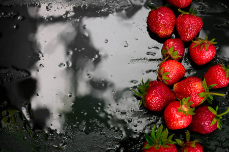 Whole strawberries on black background with water drops. Wet strawberries. Frame, copy space. Top view.の写真素材