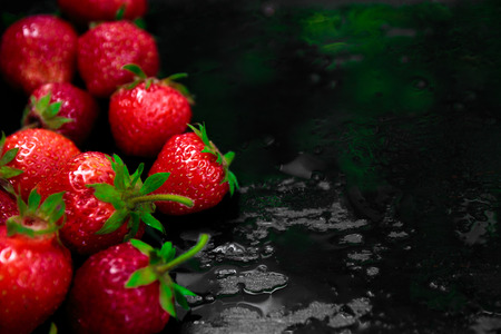 Whole strawberries on black background with water drops. Wet strawberries. Frame, copy space.の写真素材