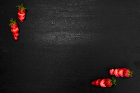 Sliced strawberries with leaves on black background. Top view, frame. Copy space. Summer fruit food frame.の写真素材