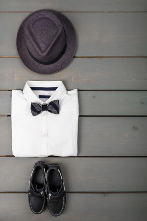 Men's outfit on wooden background. Kids fashion clothes. Grey fedora, white shirt, black bow tie and boat shoes for boy. Top view. Copy space. Frameの写真素材