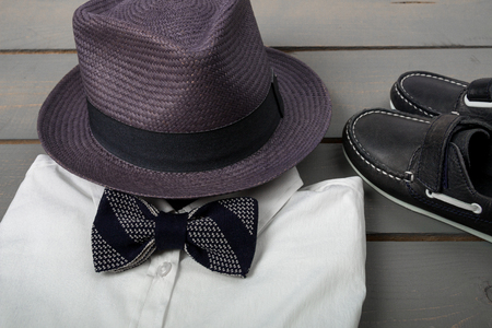 Men's outfit on wooden background. Kids fashion clothes. Grey fedora,  white shirt, balck bow tie and boat shoes for boy.  Close up.の写真素材