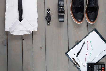 Businessman, work outfit on grey wooden background. White shirt with black tie, watch, belt, oxford shoes, planchette and calculator. Back to work. Copy space, frame. Set of mans fashion and accessories.の写真素材