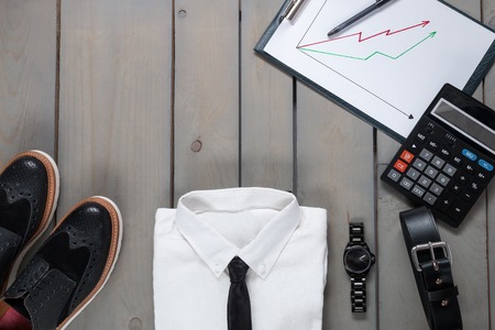 Businessman, work outfit on grey wooden background. White shirt with black tie, watch, belt, oxford shoes, planchette and calculator. Back to work.の写真素材