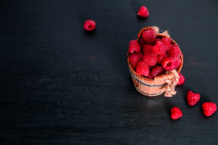 Red raspberries in a basket on black wooden background. Frame. Copy space.