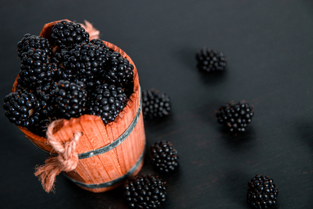 Black raspberries in a wooden basket on black wooden background. Frame. Copy space.の写真素材