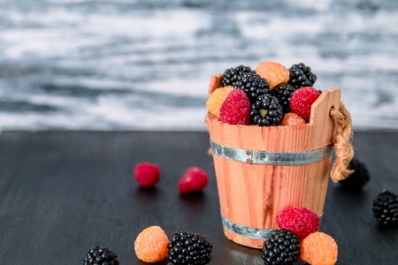 Mixed of red, black, yellow raspberries in a wooden basket and berry on black table. Close up.の写真素材