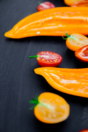 Mixed of half red and yellow pepper with a green branch near cherry tomato on a black backround. Close up.の写真素材