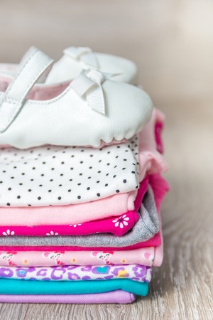 Folded pink and white bodysuit with shoes on it on grey wooden background. diaper for newborn girl. Stack of infant clothing. Child outfit. Copy space.の写真素材