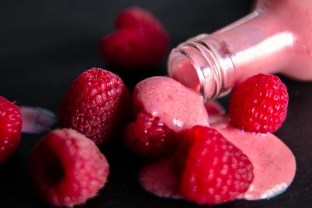 Spilled raspberry smoothie from bottle on black table near berry.の写真素材