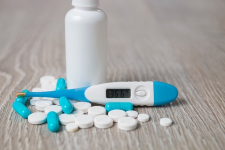 Blue and white medication, nasal spray, pills, vitamins, capsules, thermometer on grey wooden background. All for flu.の写真素材
