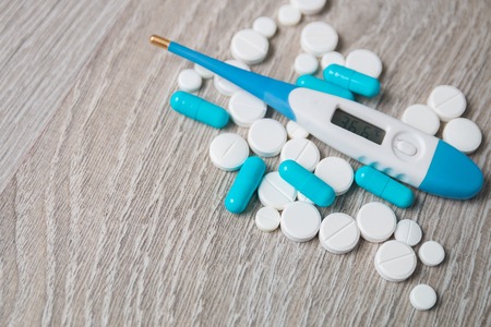 Blue and white medication, pills, vitamins, capsules, thermometer from above on grey wooden...