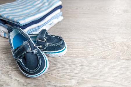 Folded blue and white bodysuit with shoes on it on grey wooden background. diaper for newborn boy. Stack of infant clothing. Child outfit. Copy space.の写真素材