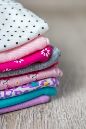 Fabric Sewing. Folded pink and white bodysuit on it on grey wooden background. diaper for newborn girl. Stack of infant clothing. Child outfit. Close up.の写真素材