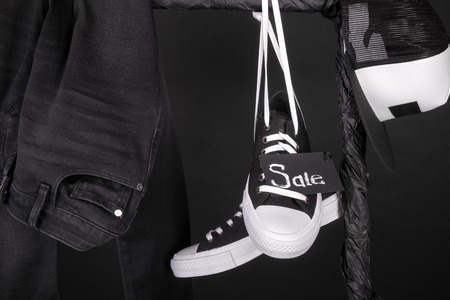 Sale sign. Black and white sneakers, cap and pant, jeans hanging on clothes rack on black background.  Black friday. Close up.の写真素材
