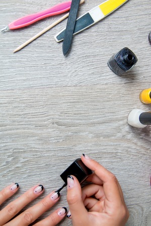 Black nail polish being applied to hand with tools for manicure on background. Beautiful manicure process.  Top view. Copy space. Frame.の写真素材