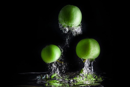 Three green apples splashing into water on black background.