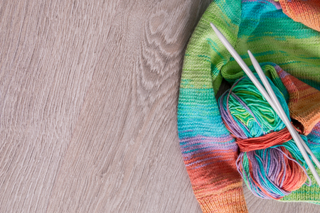 Knitting. Knitted sweater. Multicolor ball of yarn with needles near the handmade products on grey...