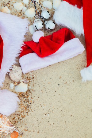 Three christmas hats on the beach. Santa hat on the sand near shells. Family holiday. New year vacation. Copy space. Frame. Top view.の写真素材