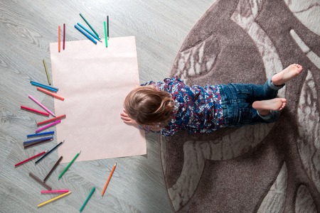 Little girl painting, drawing. Child lying on the floor near crayons. Top view. Creativity concept.の写真素材