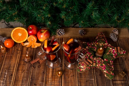 Christmas mulled wine with fruits and spices on wooden table. Xmas decorations in background. Two glasses. Winter warming drink with recipe ingredients around.の写真素材