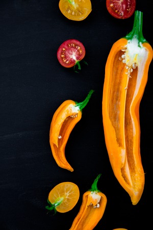 Mixed of half red and yellow pepper with a green branch near cherry tomato on a black background. Copy space.の写真素材