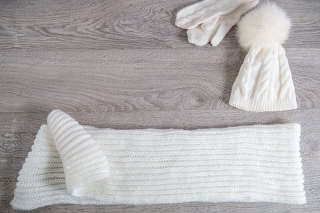 Knitted cold weather accessory on the table. White hat, scarf ant gloves on grey wooden background. Top view. Copy space.の写真素材