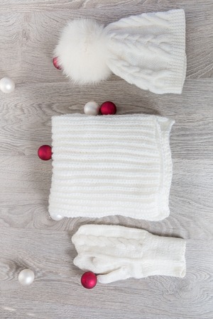 Knitted cold weather accessory near new year tree balls on the table. White hat, scarf ant gloves on grey wooden background. Top view. Christmas decoration.の写真素材
