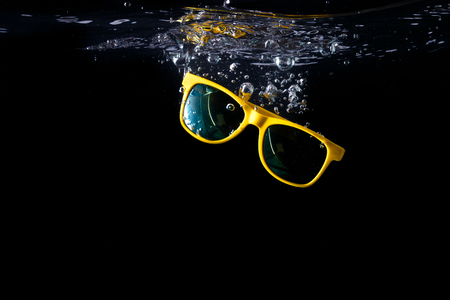 Yellow sunglasses splashing into water on black background. eyewear falling into water. Copy space.の写真素材