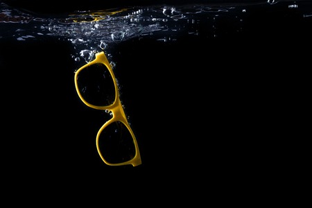 Yellow sunglasses splashing into water on black background. eyewear falling into water. Copy space.