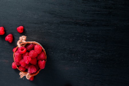 Red raspberries in a basket on black wooden background.の写真素材