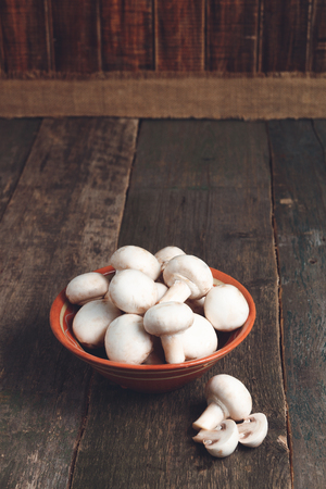 Fresh white mushrooms champignon in brown bowl on wooden background.の写真素材